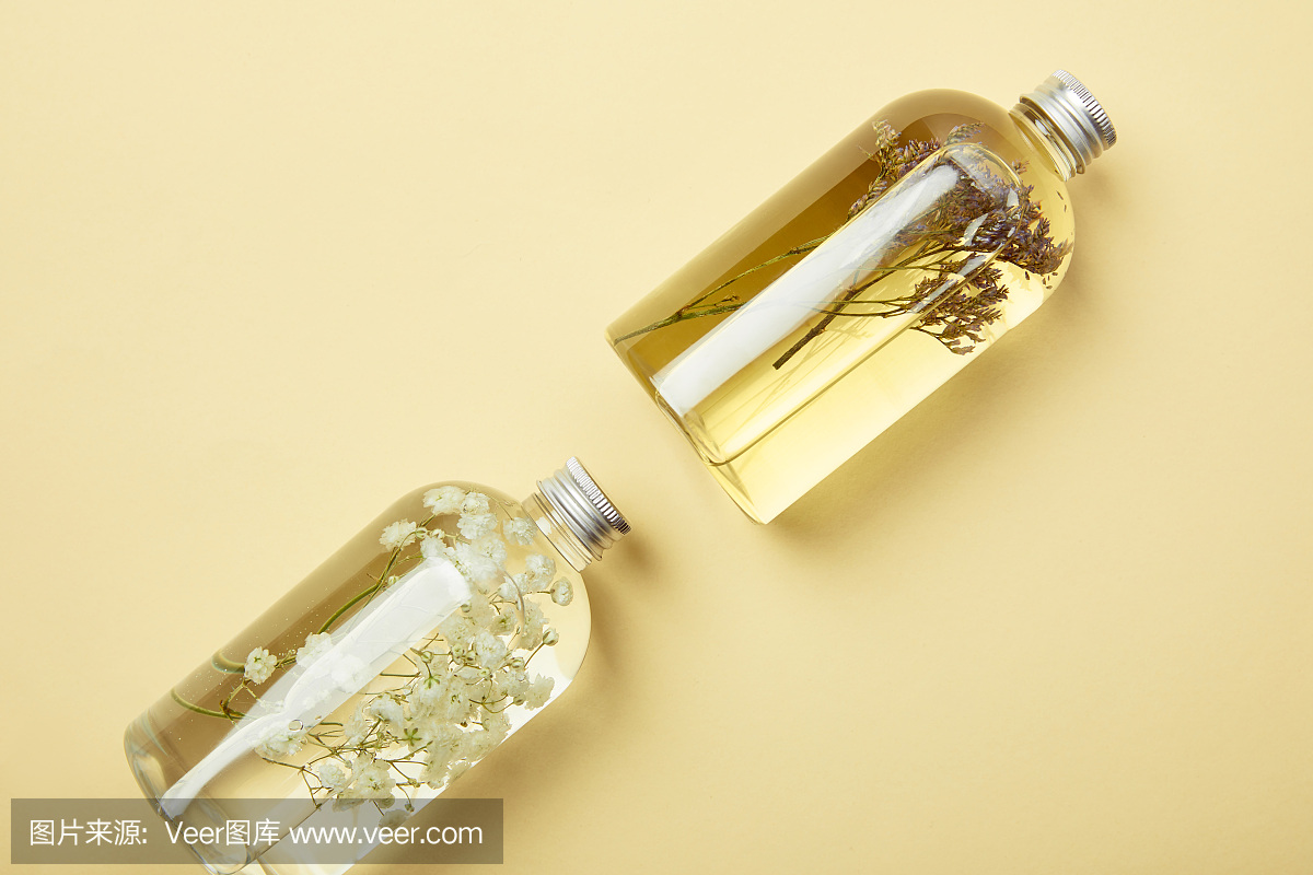 俯视图的透明瓶与天然液体美容产品和野花在黄色的背景